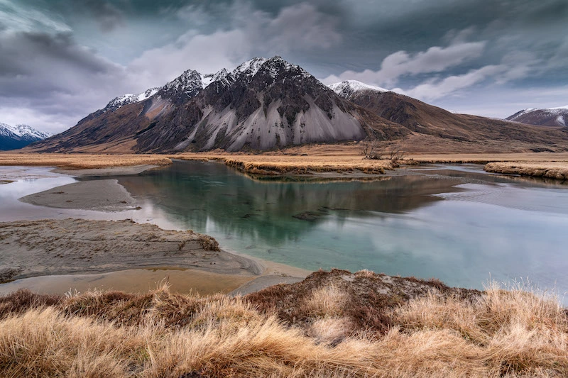 Photographie d'une montagne entourée d'un lac avec un ciel sombre