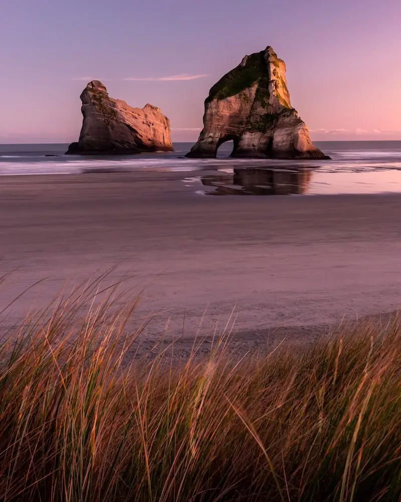 Photographie de la plage de Wharariki sous un coucher de soleil rose, Nouvelle-Zélande