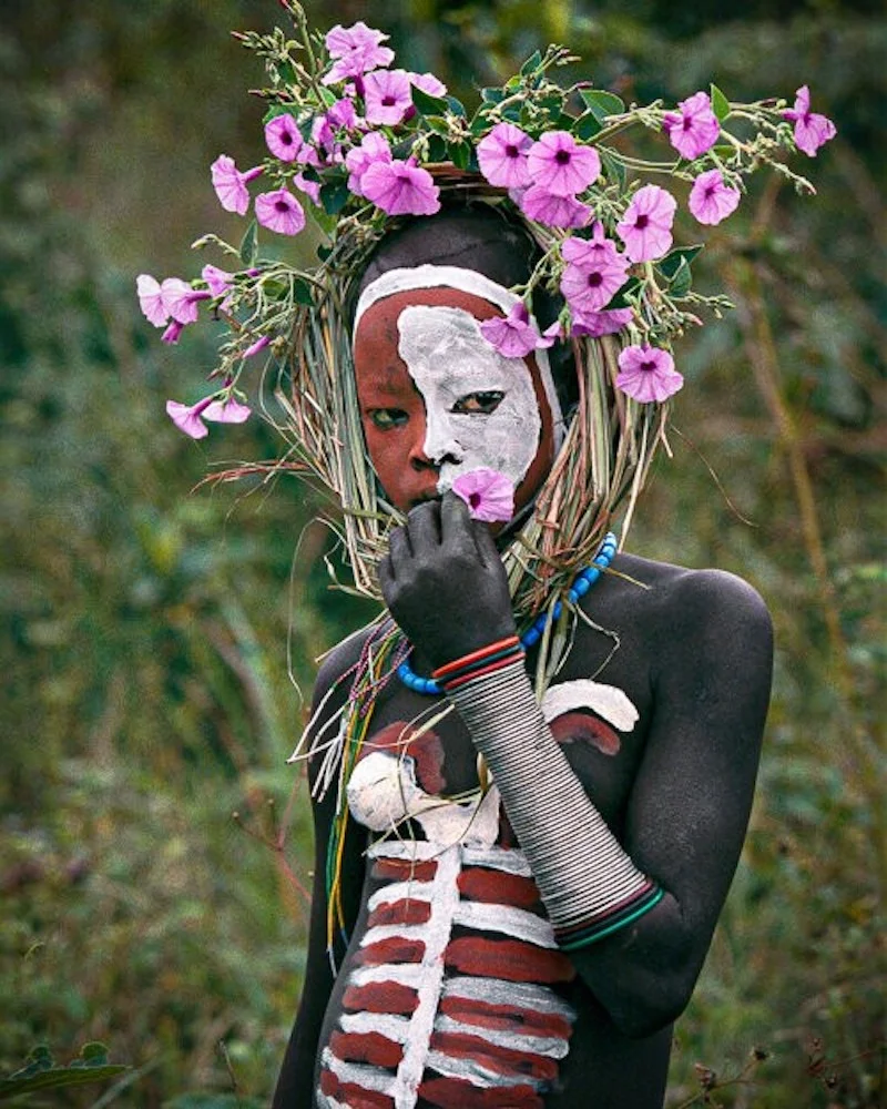 Portrait of a woman in Ethiopia with tribal paintings on her body and pink flowers on her head, taken by Hans Silvester