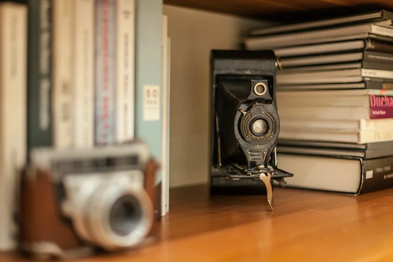 Silver cameras on a bookshelf with books