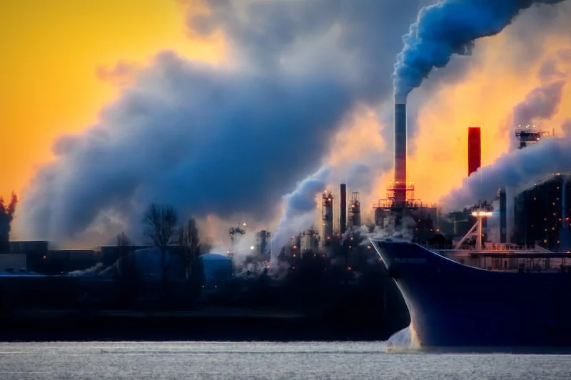 Photography of smoke coming out of factories with an orange sky behind showing an impact of digital on climate