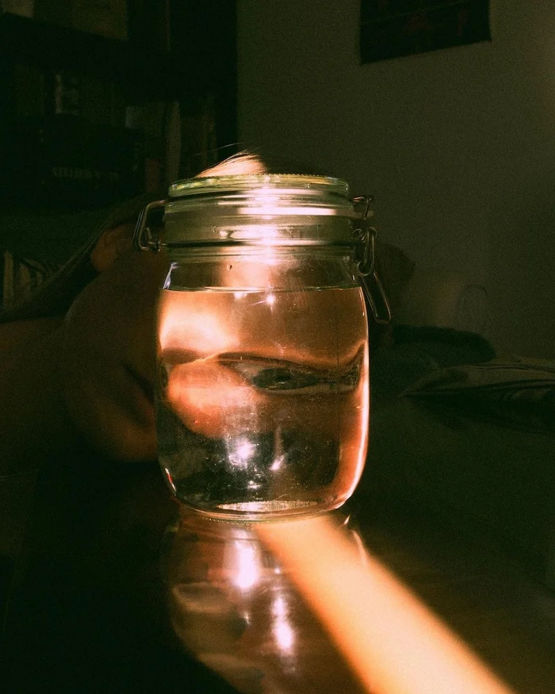 Photo d'artiste d'un pot d'eau avec un visage derrière, éclairé par la lumière dans une pièce sombre, prise lors du confinement.