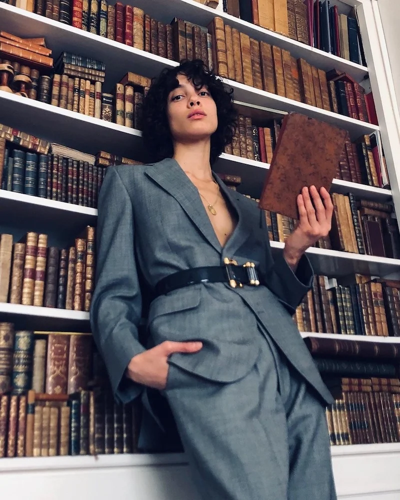 A woman leaning over a bookshelf, holding a book with her hand