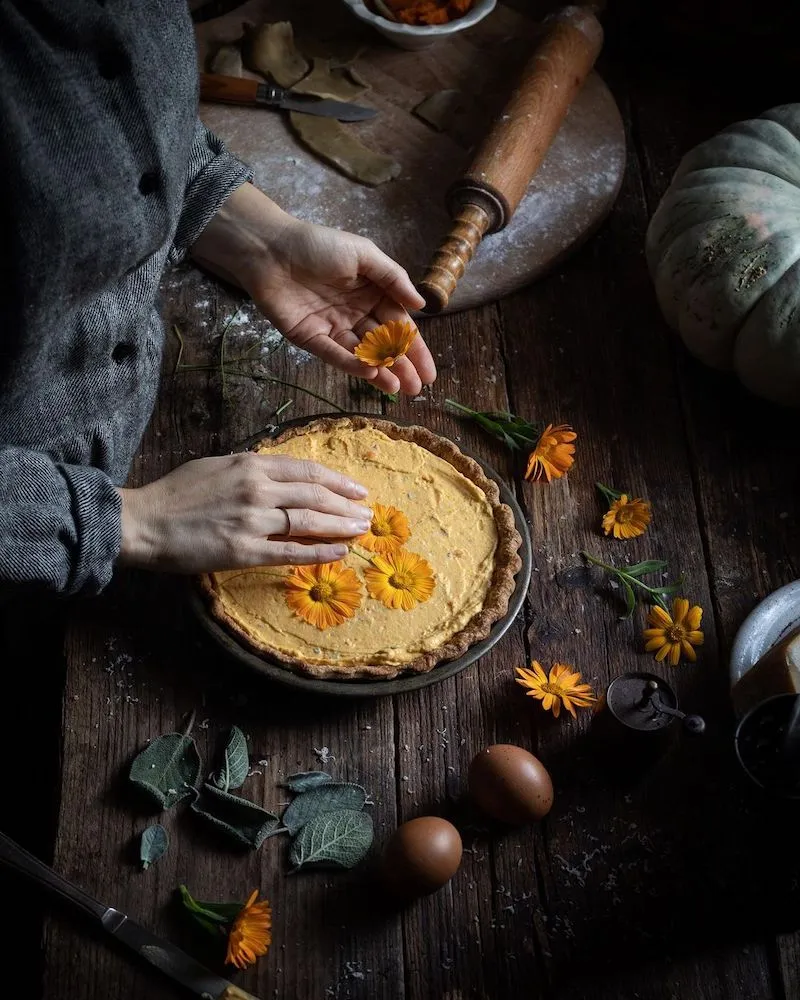 Photographie d'une personne préparant une tarte avec des fleurs oranges sur le dessus