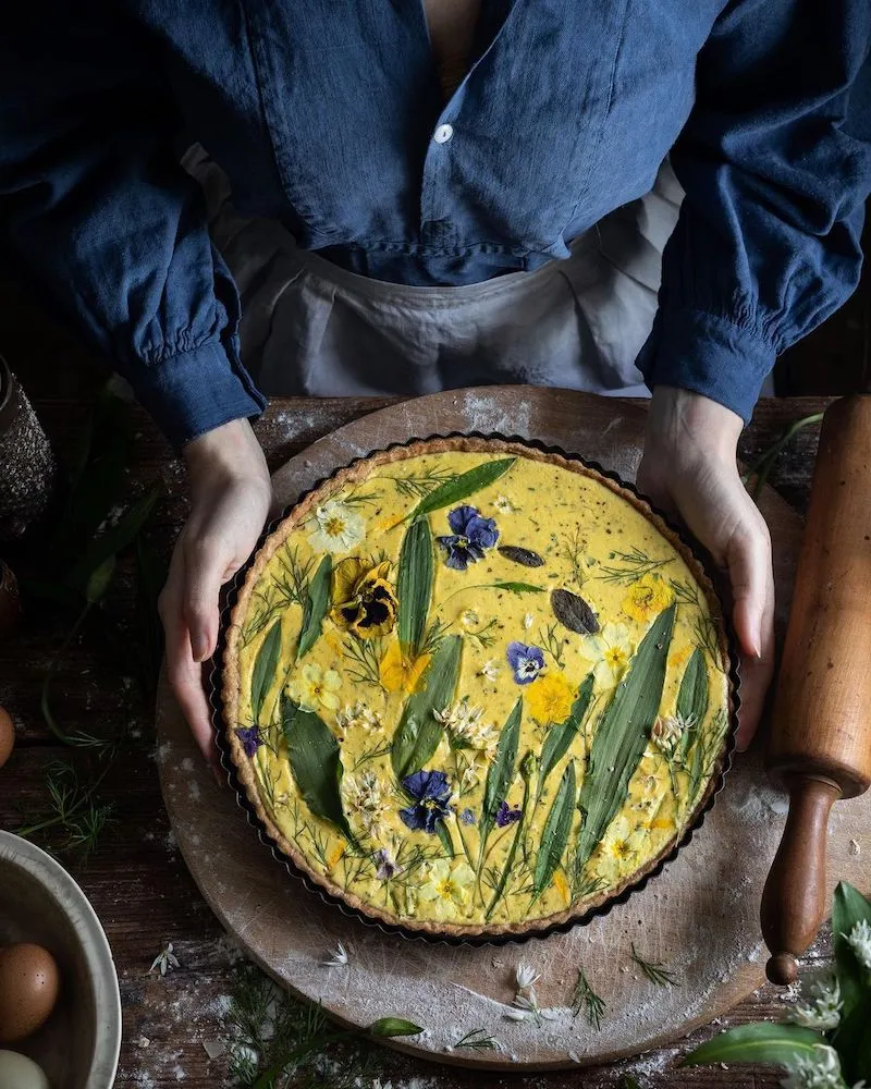 Photography of someone holding a pie covered in flowers and stems, taken by Aimee Twigger, food photographer