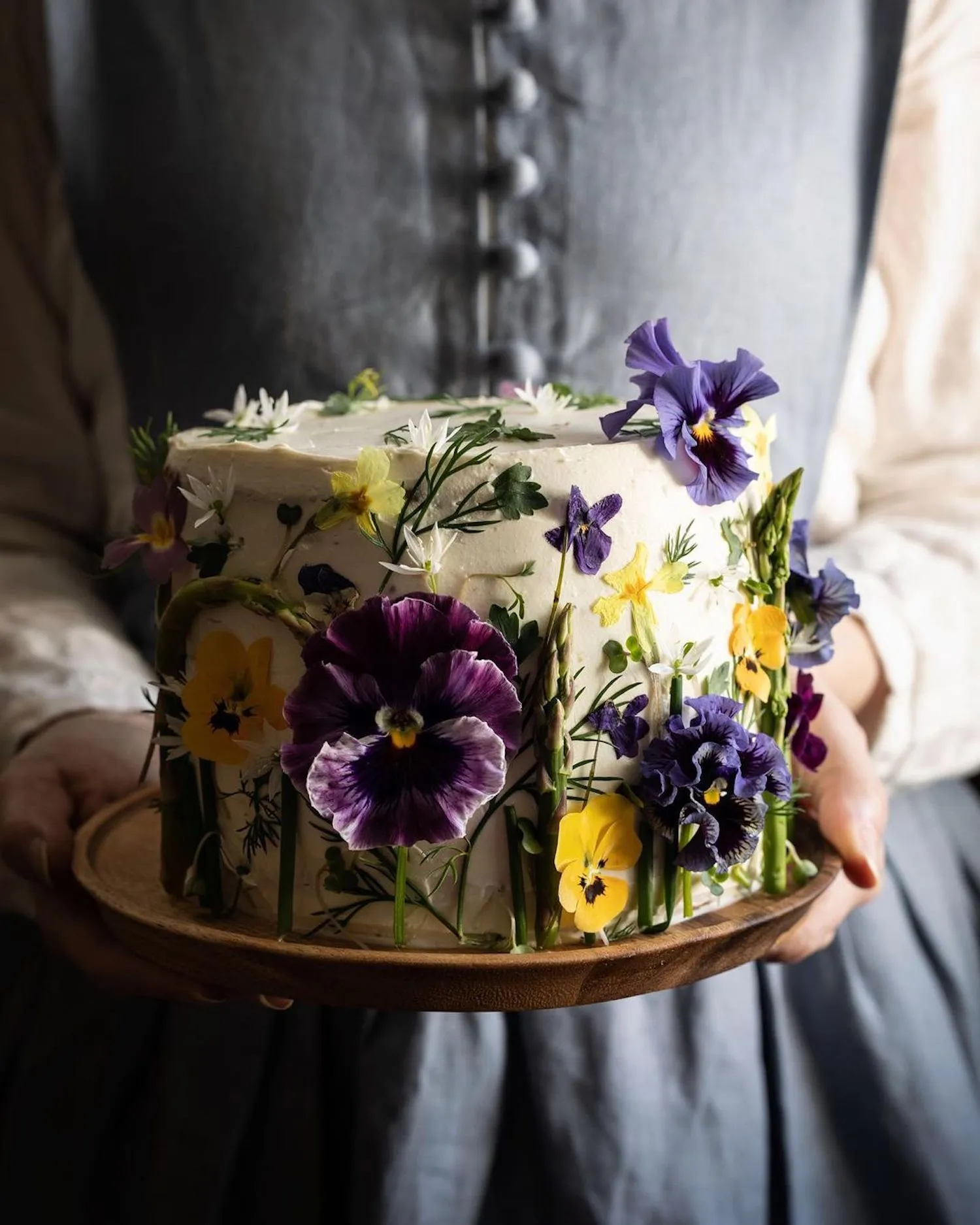 Photography of someone holding a cake covered in yellow and purple flowers, taken by Aimee Twigger, food photographer