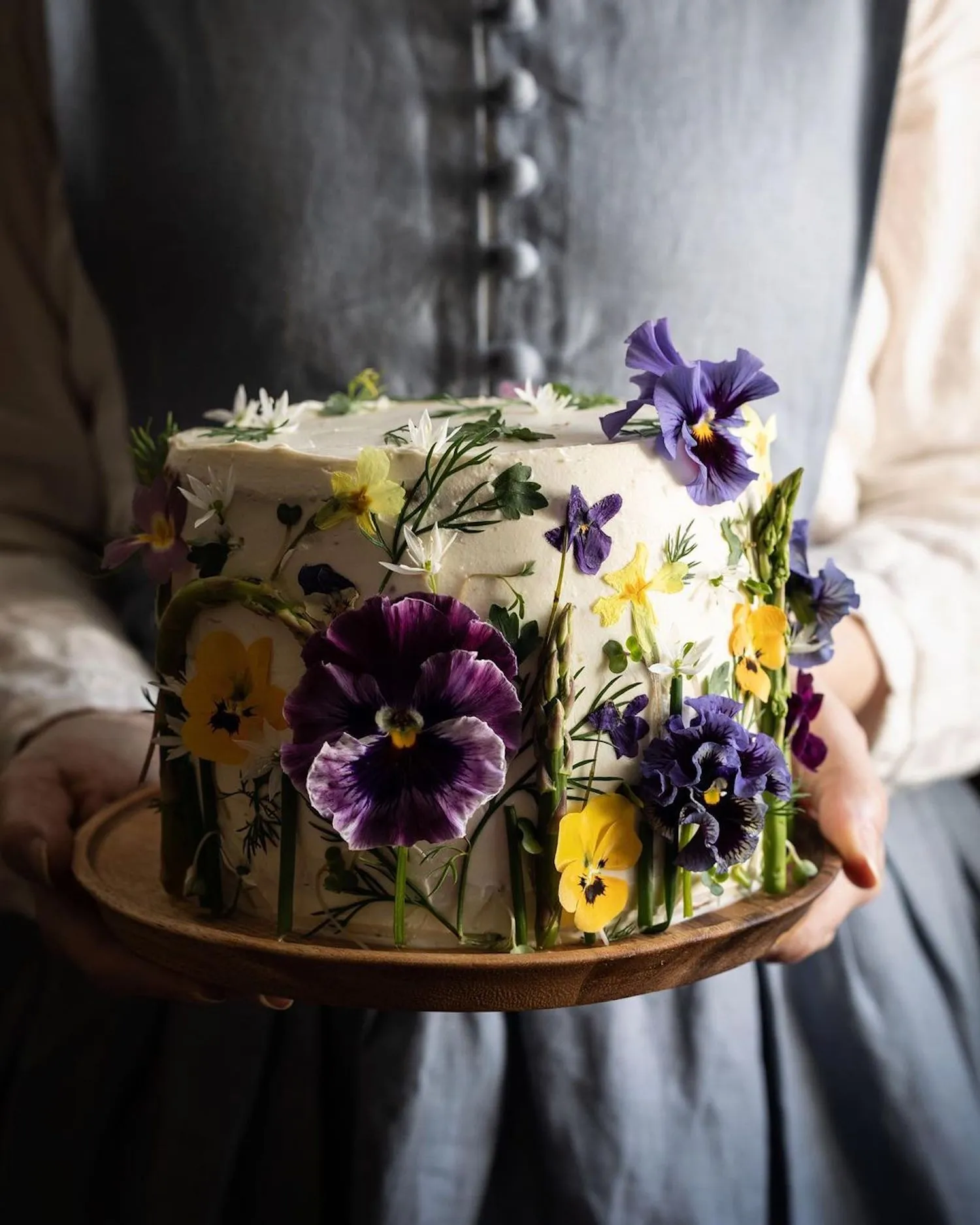 Photographie d'une personne tenant un gâteau couvert de fleurs jaunes et violettes, prise par Aimee Twigger, photographe culinaire