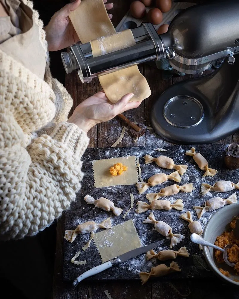 Photographie d'une personne préparant des pâtes avec des raviolis en forme de bonbons sur la table