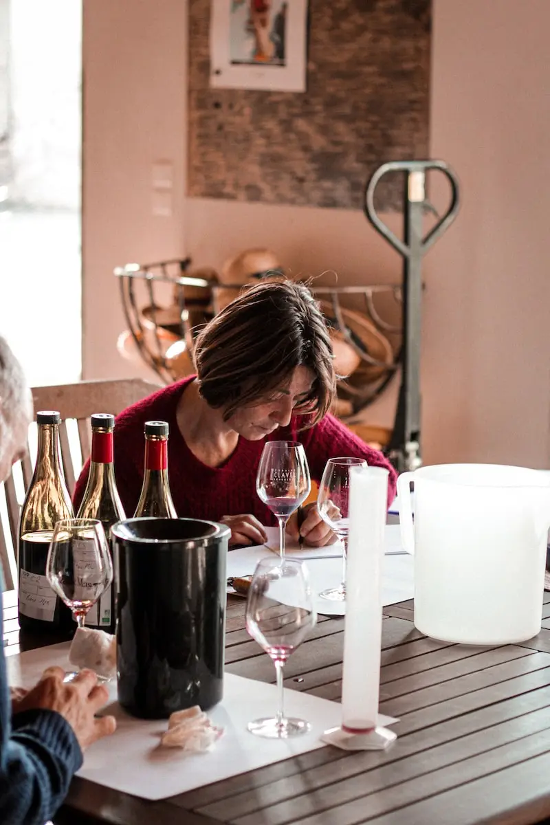 Photographie d'une femme prenant des notes à côté de bouteilles et de verres de vin au Domaine Clavel