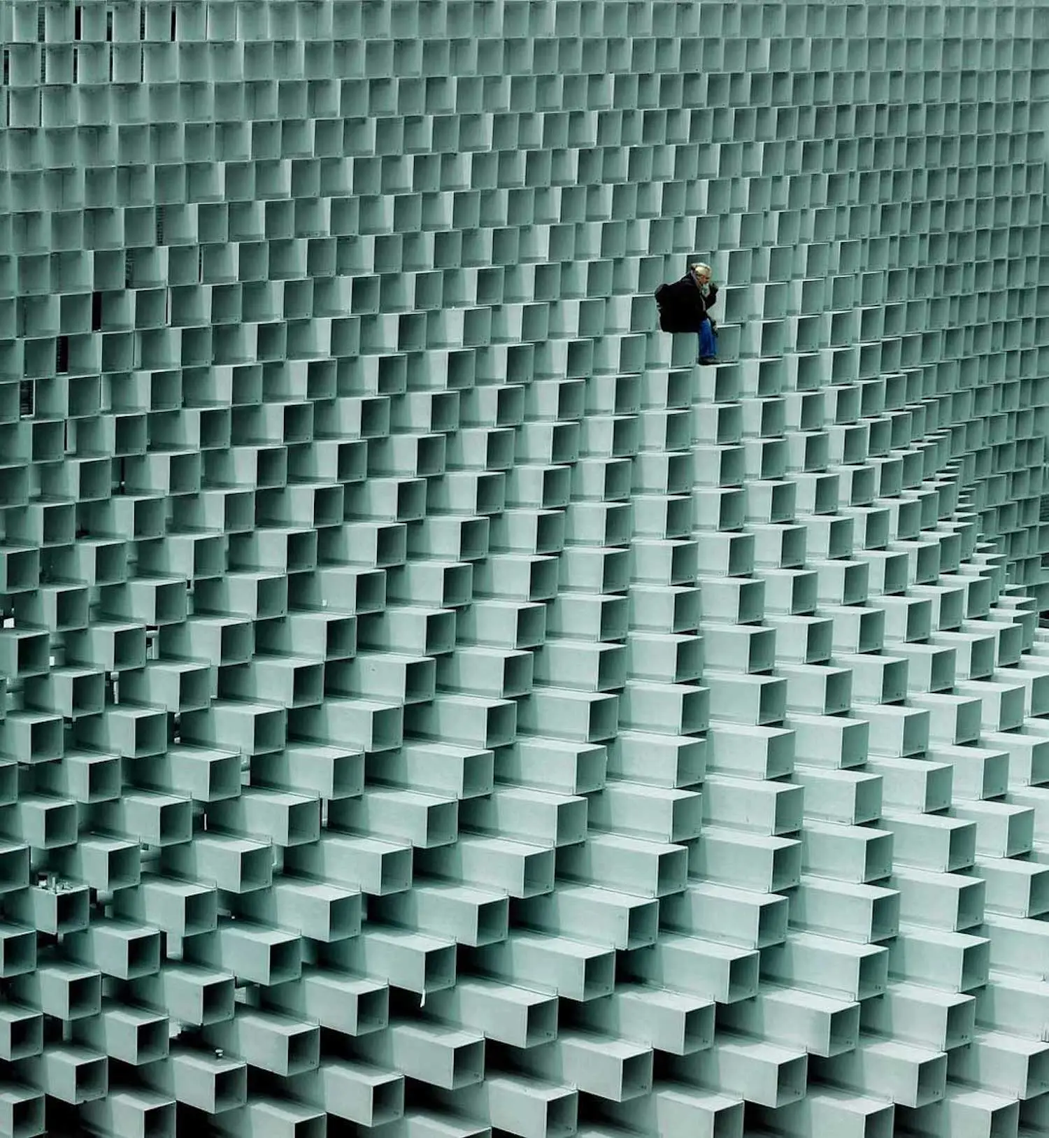 Photographie d'un ouvrier sur un bâtiment fait de prismes rectangulaires blancs