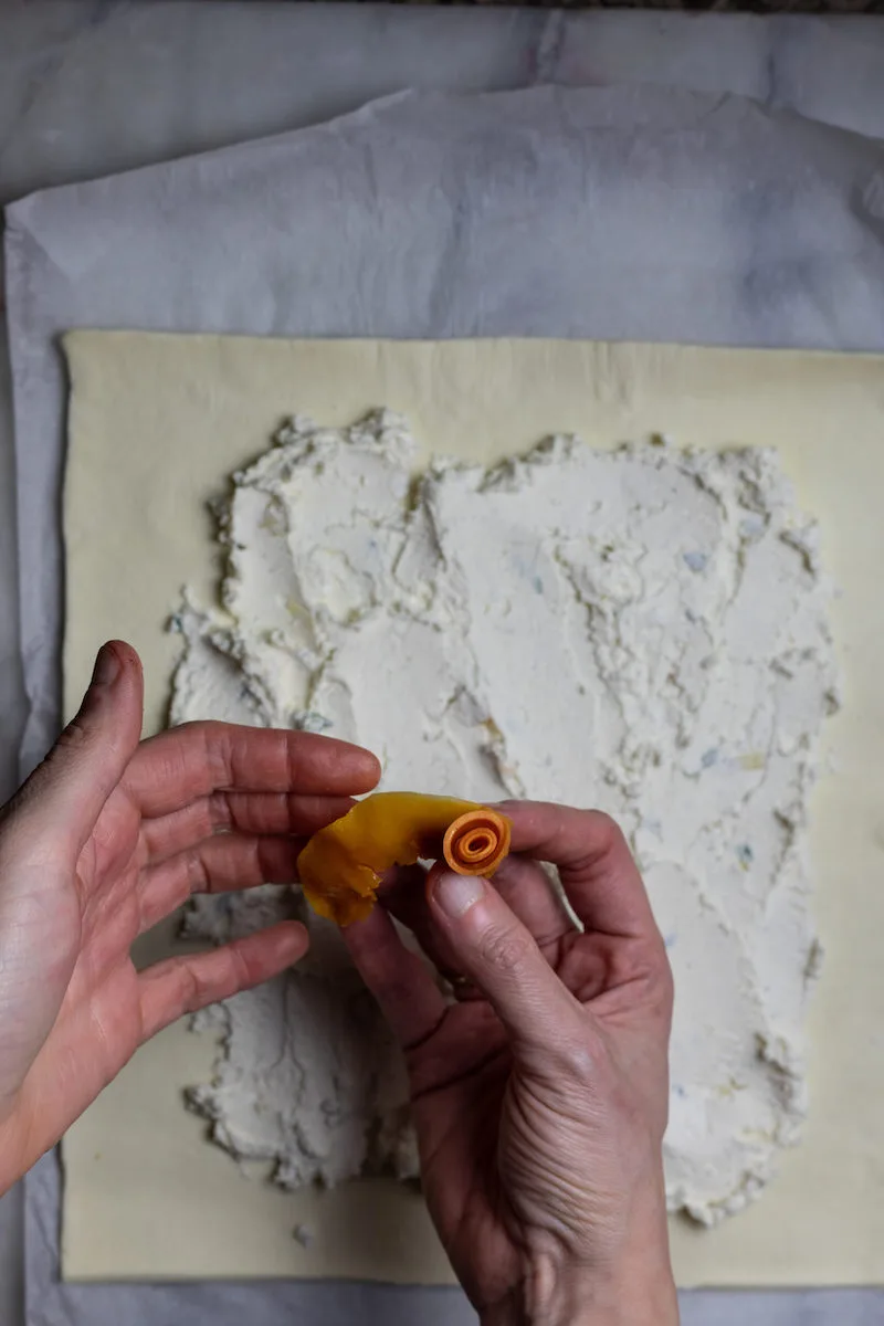 Photographie d'une personne créant une rose à partir d'aliments, avec de la pâte feuilletée et de la farine en arrière-plan.