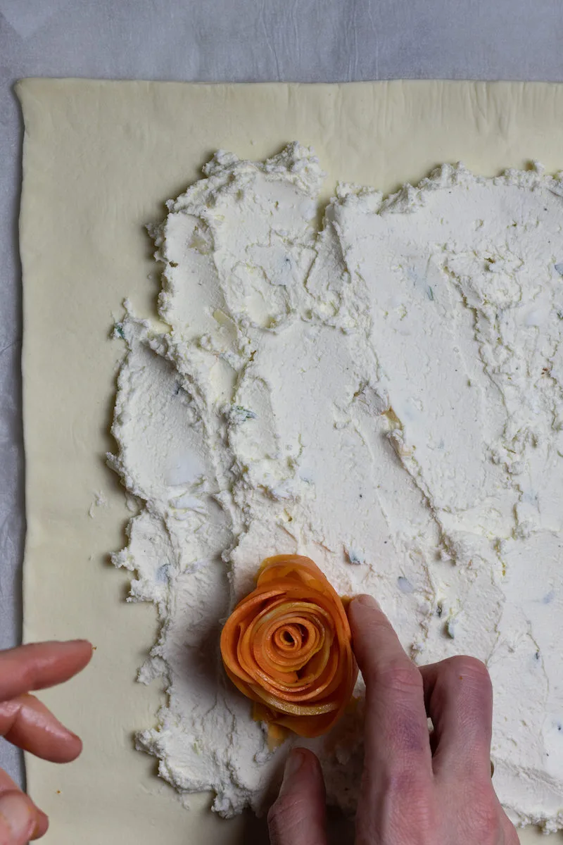 Photographie d'une personne créant une rose à partir d'aliments, avec de la pâte feuilletée et des farines en arrière-plan